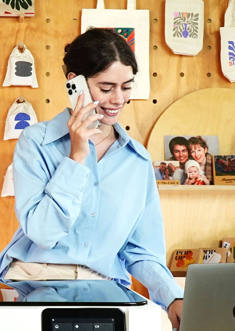 Nasmejana preduzetnica telefonira, u pozadini su primeri FLUX Ador radova.