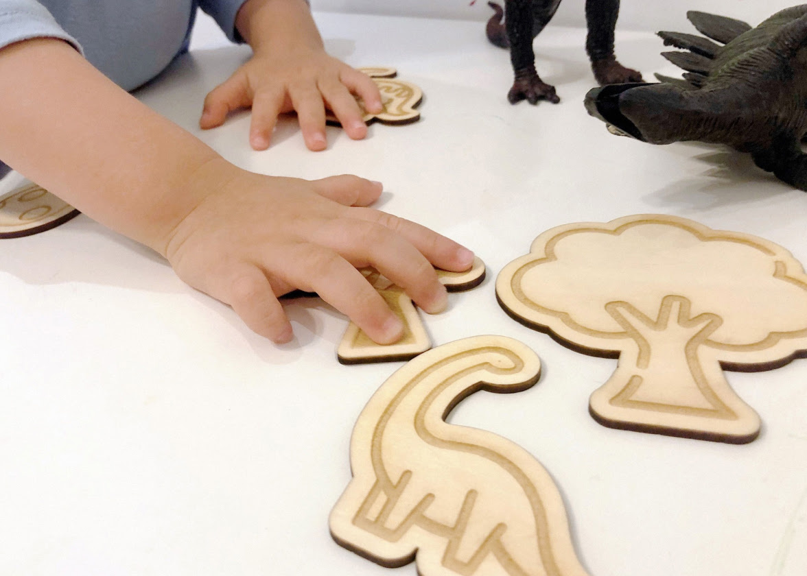 Dete drži laserski isečene i gravirane drvene figure dinosaurusa i drveća.